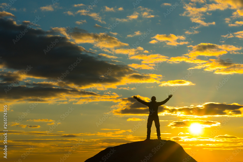 Silhouette of a man at the top of the mountain, against the backdrop of the sunset. Happy, hands raised, winner