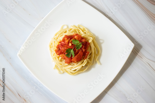 Pasta with fresh tomatoes, cooked with olive oil and garlic on a light background and a white square plate. Italian food. Horizontal orientation