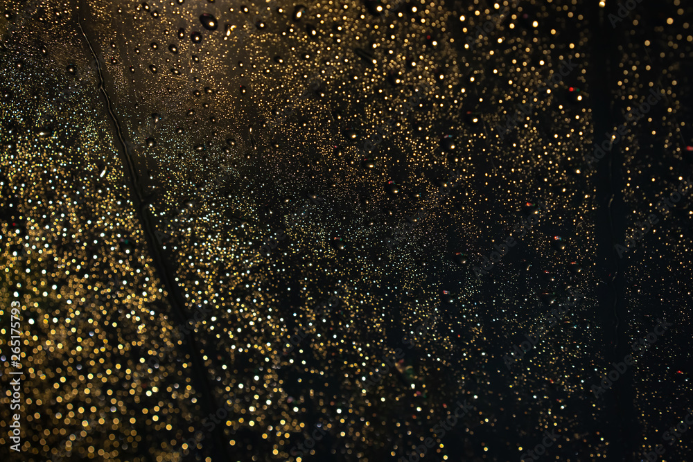 Fototapeta premium Beautiful rain drops on car glass while heavy traffic jam at night. Beautiful rain drop on glass background with colorful lighting from a cars and street.