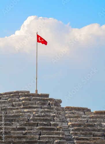 Turkish flag on top of an ancient amphitheater against the backdrop of a large cloud close-up