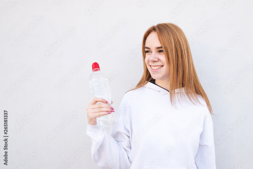 Fitness model holding a water bottle in in hand, looking sideways and smiling. Happy sporty girl with a bottle of water in hands, smiling, isolated on white background. Healthy drink and sport concept Fitness model holding a water bottle in in hand, looking sideways and smiling. Happy sporty girl with a bottle of water in hands, smiling, isolated on white background. Healthy drink and sport concept