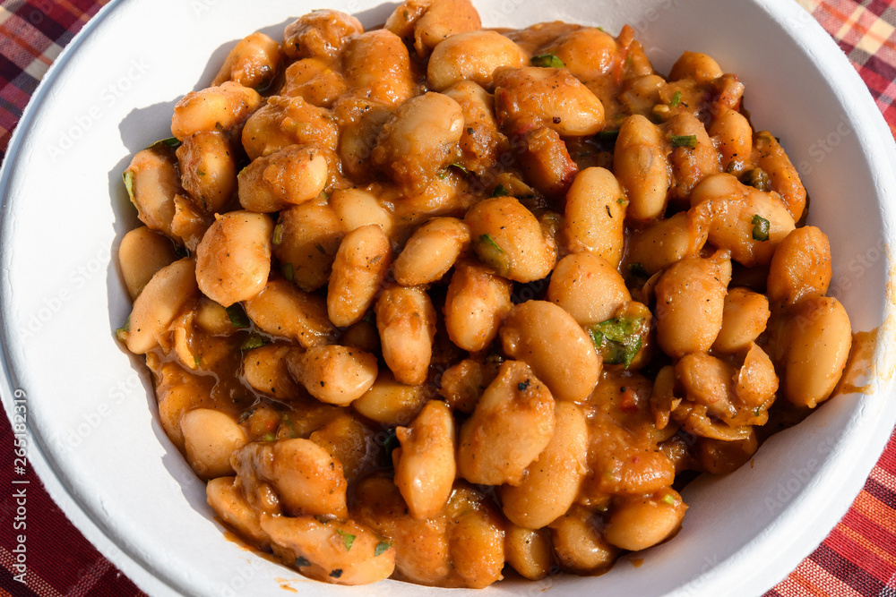 Close of a large portion of white beans cooked with tomato sauce and hot spices in display at a street food market Close of a large portion of white beans cooked with tomato sauce and hot spices in display at a street food market