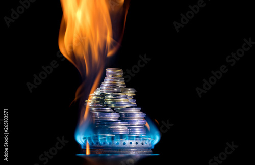 Coins on fire. The concept of high prices for natural gas. Blue flame of burning natural gas from a gas stove with Ukrainian coins.