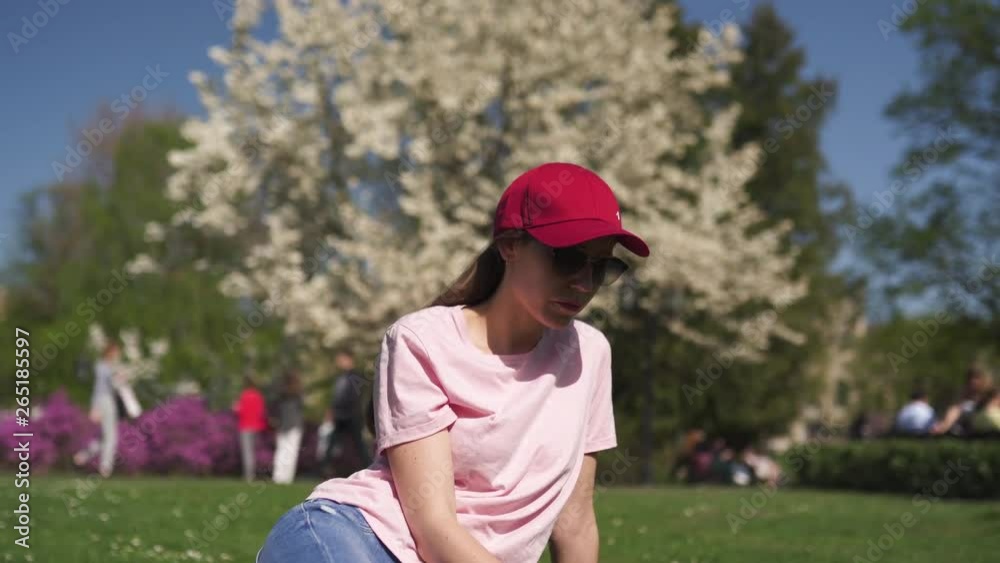Successful business woman enjoys her leisure free time in a park with blossoming sakura cherry trees wearing jeans, pink t-shirt and a fashion red cap Successful business woman enjoys her leisure free time in a park with blossoming sakura cherry trees wearing jeans, pink t-shirt and a fashion red cap