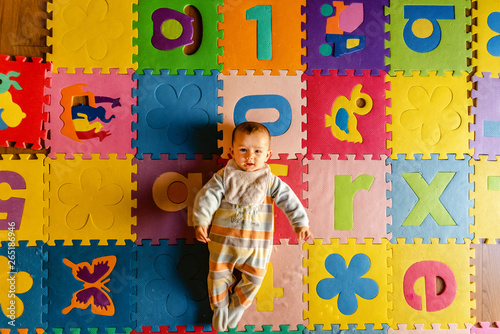 Adorable smiling baby seen from above in pajamas  lying on his back in his toy room.
