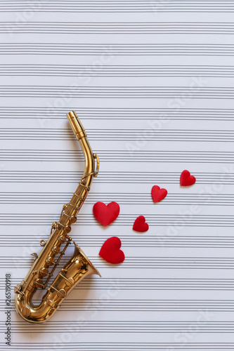 Little Golden saxophone and Red heart shape figurines.. . Top view  close-up on note paper background