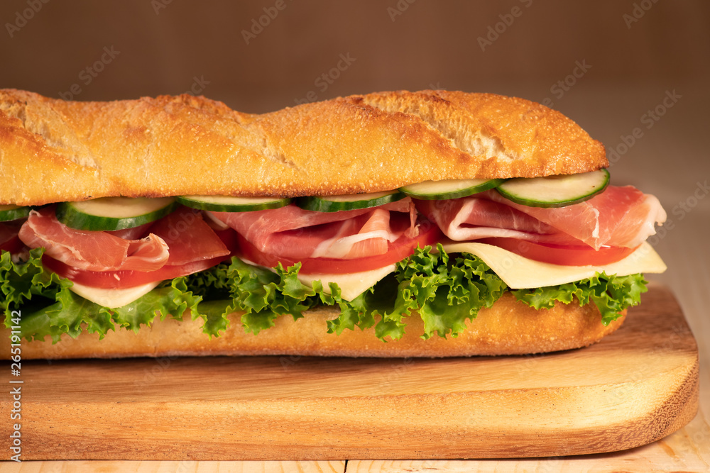 Fresh crispy sandwich with prosciutto, cheese, tomatoes, lettuce, cucumbers on a wooden background.Close Up. Healthy concept.