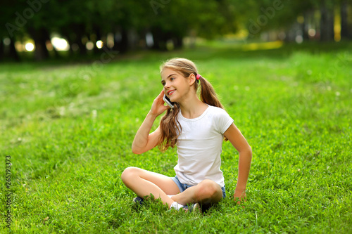 Foto Charming teen girl in shorts and t-shirt in summer sitting on the grass and talk