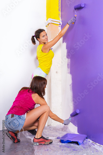 young beautiful women paints white wall with purple paint roller