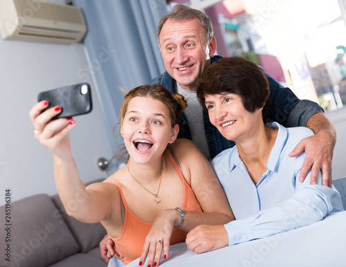 Marrieds with their adult daughter are takinf selfie together on sofa photo