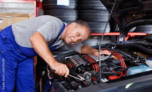 Professional mature man car mechanician repairing car in auto repair shop