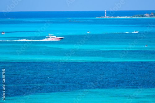 Bote deportivo navegando por el mar caribe con personas disfrutando de un día soleado en el mar caribe de Cancun, Mexico, contraste de colores azul turquesa y faro de navegación al fondo