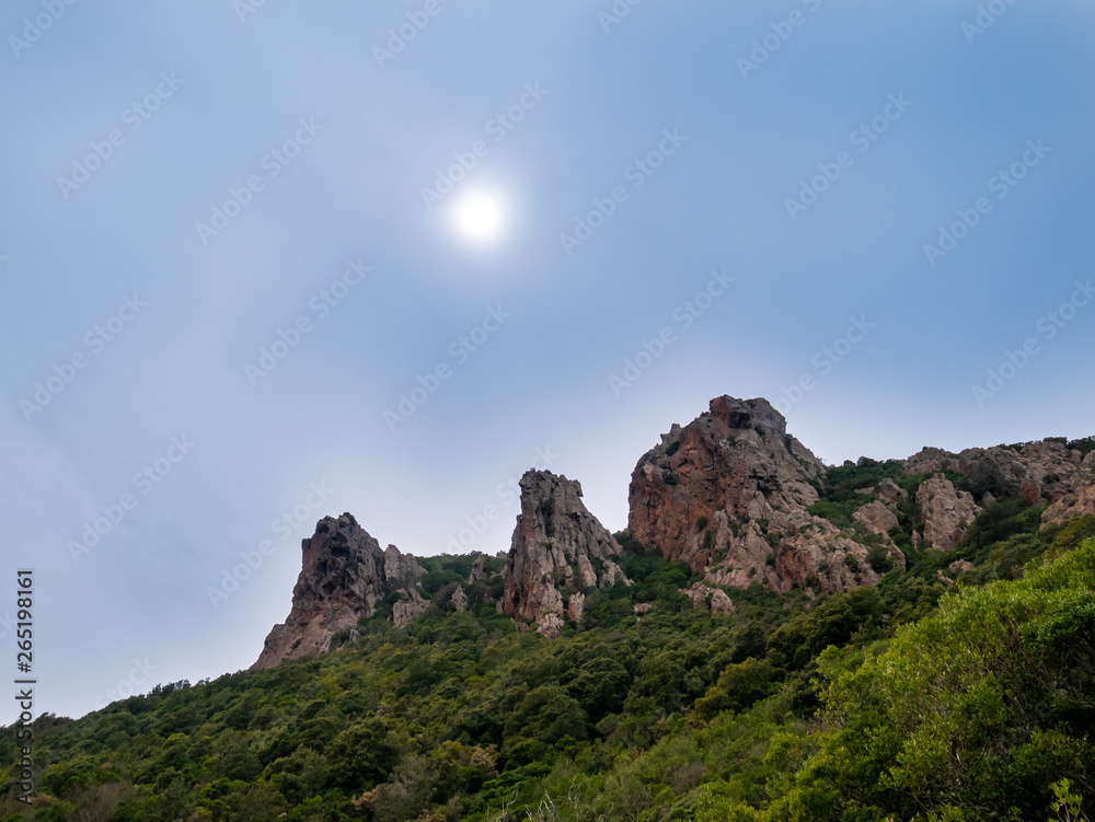three mountain peaks with sun shining through the mist. path from Galeria to Girolata. panorama of Scandola Nature Reserve a Natural World Heritage Site, Corsica Regional Park, France