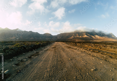 Long off road terrain way road viewed from ground level with mountains and blue cloudy sky - travel and adventure concept for alternative vacation and lifestyle