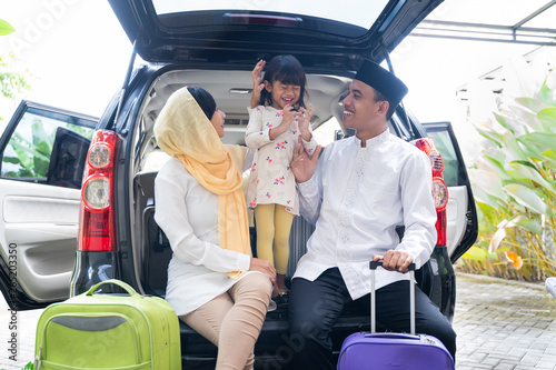 muslim family with kid sitting in the car trunk with suitcase. eid mubarak or idul fitri mudik