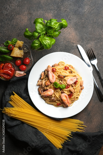 Seafood pasta and dried tomatoes in a creamy sauce with basil and parmesan on a dark background.