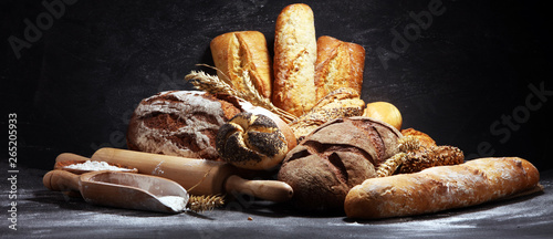 Assortment of baked bread and bread rolls on rustic black bakery table background