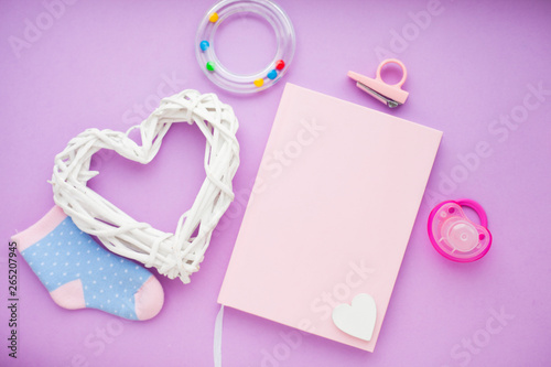 Newborn baby story. Strow heart and children's toys, scissors, baby bottle, nipple, hairbrush on violet background