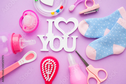 Newborn baby story. Strow heart and children's toys, scissors, baby bottle, nipple, hairbrush on violet background