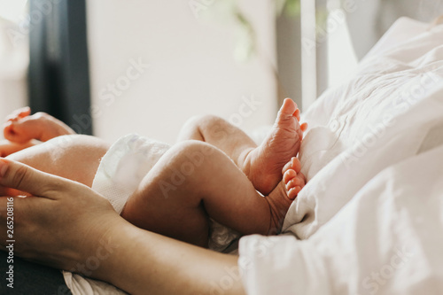 legs of a newborn baby in the arms of his mother