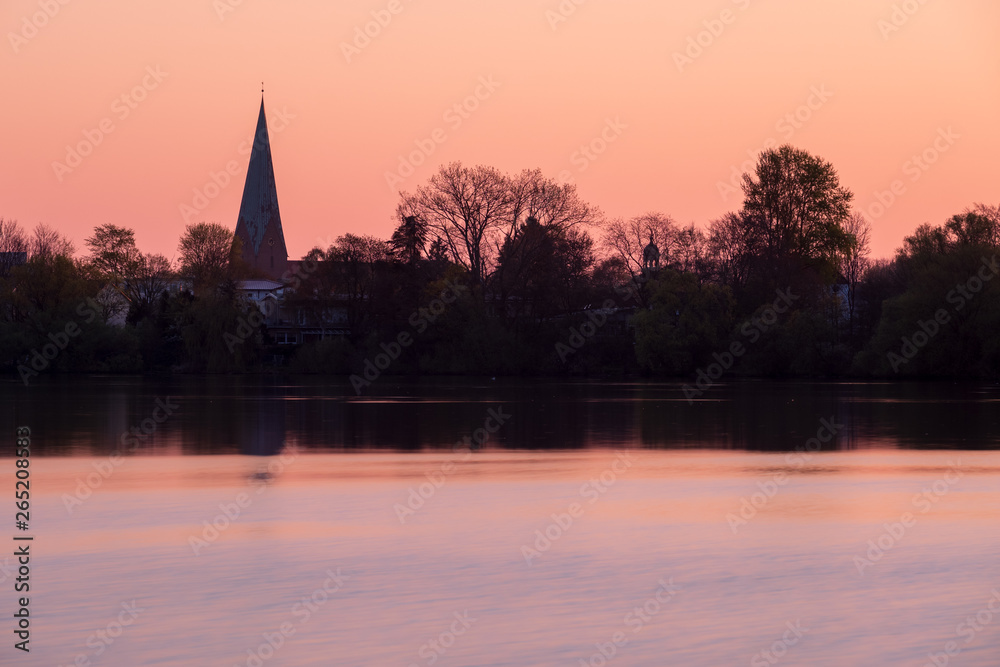 Silhouette der Stadt Eutin am Sonnenaufgang über kleinem See mit Turm der Michaelis-Kirche, Schleswig-Holstein