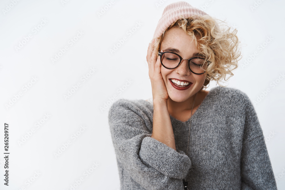 Tenderness, winter and sensuality concept. Gentle good-looking flirty girlfriend with curly short blond hair in beanie, glasses, cozy sweater smiling with love and delight touching cheek, close eyes Tenderness, winter and sensuality concept. Gentle good-looking flirty girlfriend with curly short blond hair in beanie, glasses, cozy sweater smiling with love and delight touching cheek, close eyes
