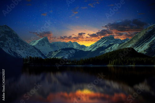 Sunset over snow covered mountains outside of Banff National Park with a lake reflection.