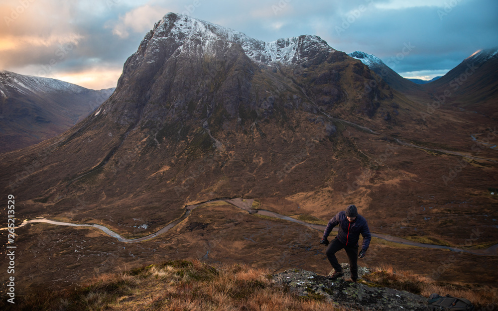 Man climbing up mountain in Scotland with valley below Man climbing up mountain in Scotland with valley below