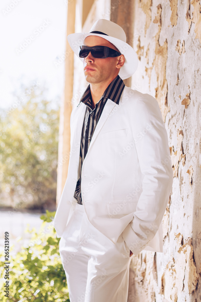 Fancy fashionable man with black sunglasses , white hat and white summer suit posing. Fancy fashionable man with black sunglasses , white hat and white summer suit posing.