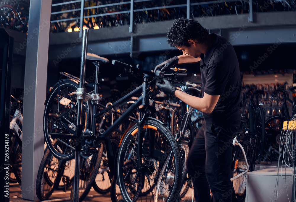 Diligent young mechanic is repairing customer's bicycle at workplace.