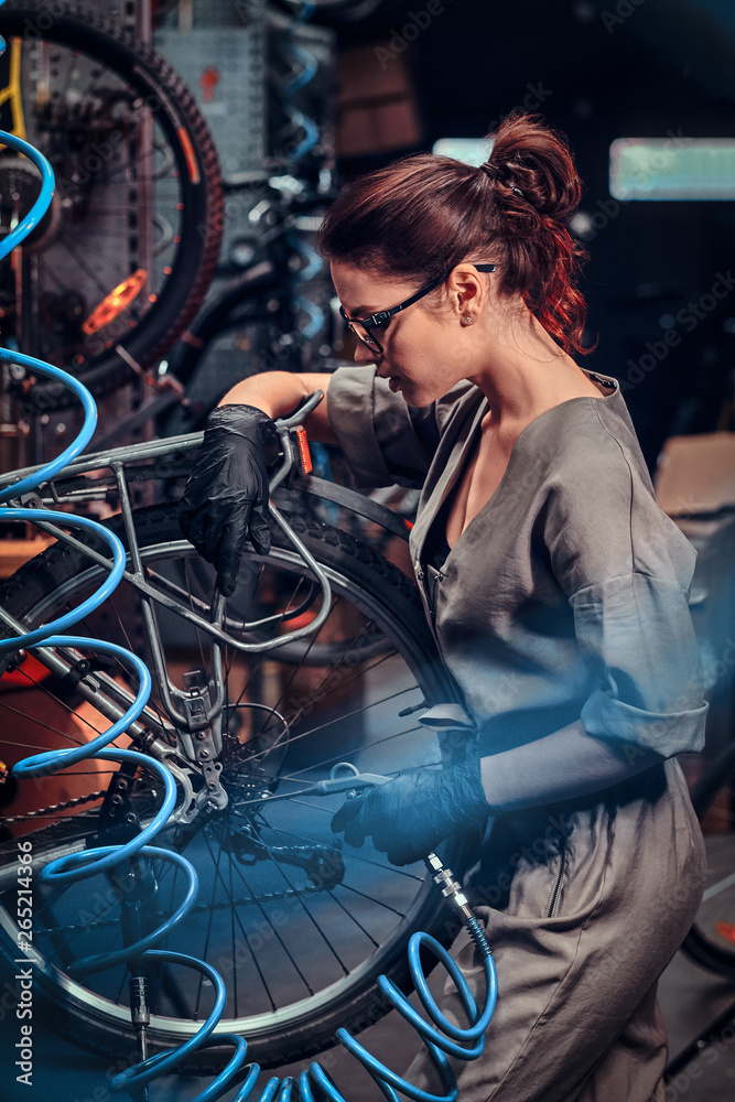 Diligent beautiful girl is repairing bicycle at busy workshop. Diligent beautiful girl is repairing bicycle at busy workshop.