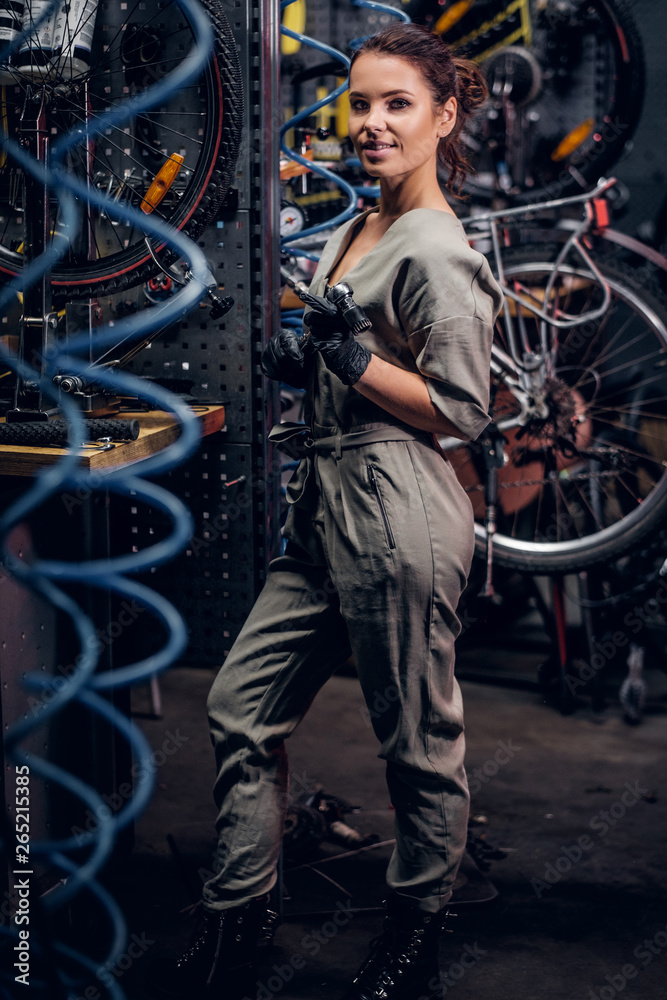 Diligent attractive woman is fixing bicycle at busy workshop in between pneumatic wires.