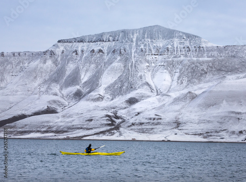Kayaker moving past snow covered hills