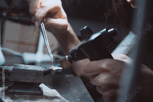 In the workshop, a woman jeweler is busy soldering jewelry