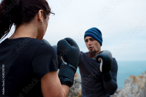 Man and woman in boxing gloves punching each other while standing on cliff against sea and cloudless sky photo