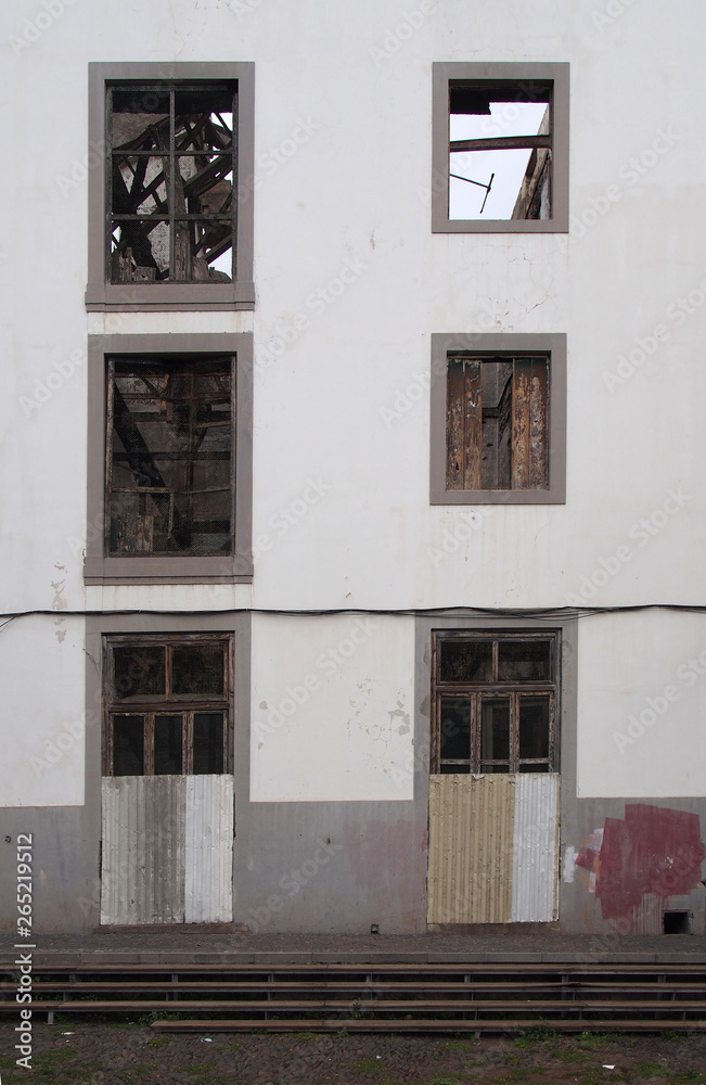 the facade of an abandoned large white industrial building with boarded up doors and empty windows shoring the wrecked roofless interior