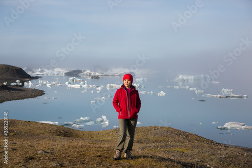girl in a red jacket is standing at sunrise against the backdrop of a glasser lagoon in the fog.