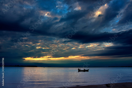 Fishing boat on the river during a cloudy and dramatic sunset 