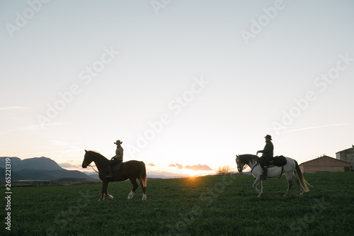 Man and woman riding horses against sunset sky on ranch