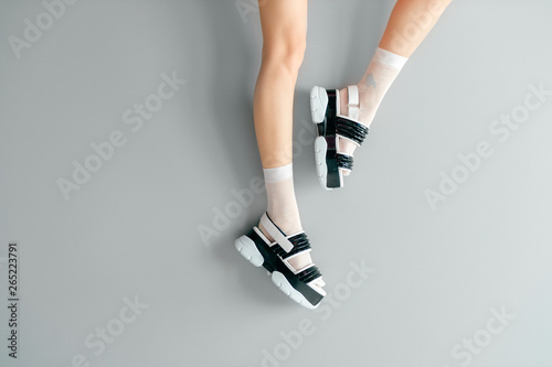Beautiful female legs in white mesh trendy socks wearing fashionable black white high wedge leather sandals. Womens modern fashion footwear. Rebel girl in high sole stylish shoes on gray background.