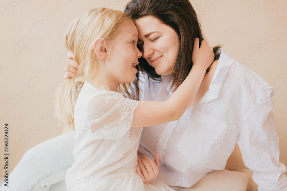 Mother and daughter indoor lifestyle portrait. Mom with child have fun in studio on yellow wall. Happiness of motherhood. Mother hugs with her little daughter. Young emotional girl embraces her mom. Mother and daughter indoor lifestyle portrait. Mom with child have fun in studio on yellow wall. Happiness of motherhood. Mother hugs with her little daughter. Young emotional girl embraces her mom.