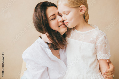 Mother and daughter indoor lifestyle portrait. Mom with child have fun in studio on yellow wall. Happiness of motherhood. Mother hugs with her little daughter. Young emotional girl embraces her mom.