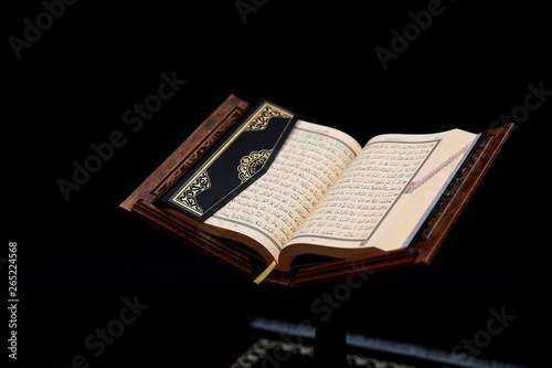 Islamic Holy Book Quran on wood carving rahle with rosary beads and prayer rug on black background. Kuran the holy book of Muslims. Ramadan concept. photo