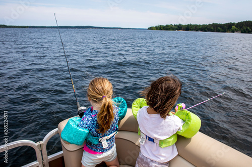 Two toddler aged girls fishing while sitting on a boat out on a lake.