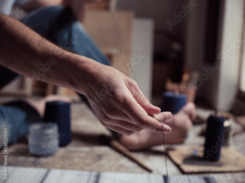 Unrecognizable male artist preparing thin dark thread while creating abstract painting on floor of workshop photo