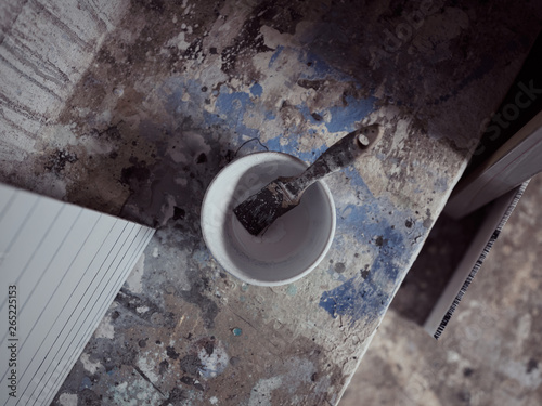 Ceramic bowl and dirty paintbrush placed on concrete ledge near abstract paintings in grungy artist studio photo