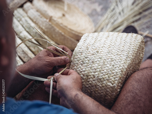 Hands of anonymous artisan showing lovely basket with floral ornament braided from dried palm fiber