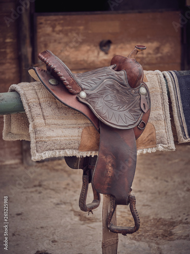 Retro leather saddle and soft pads hanging on beam near stable on ranch photo