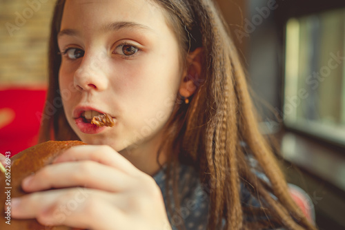 Portrait of little girl in fast food fast food restaurant, teen eating hamburger. Happy child eating unhealthy food at the restaurant. girl eating a cheeseburger in a cafe