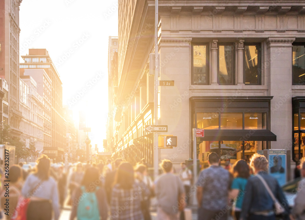 Crowd of anonymous people walking down the busy sidewalk on 23rd Street in Manhattan, New York City with bright light of sunset